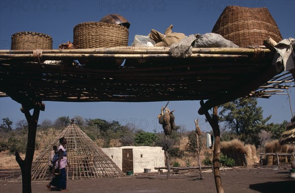 SENEGAL, Buildings, "Family enclosure with circular hut beside frame of roof, passing woman and raised platform in foreground with sacks and baskets on top."