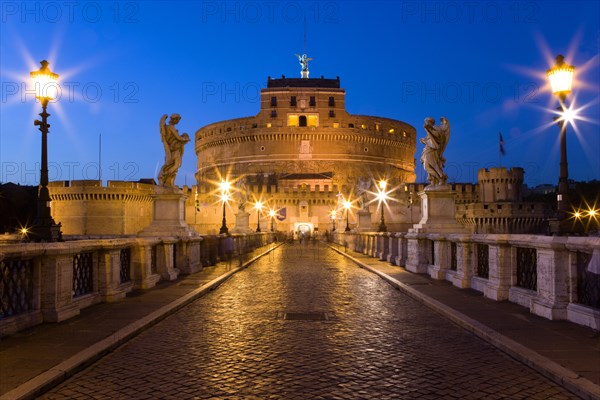 ITALY, Lazio, Rome, The 3rd Century bridge Ponte Sant'Angelo lined with statues and the 13th Century Castle of Castel Sant'Angelo on the banks of the Riber Tiber illuminated at dusk. Originally the mausoleum of Emperor Hadrian it became the residence of Popes in times of unrest linked to the Vatican by a viaduct