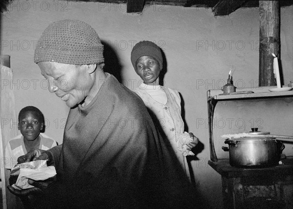 SOUTH AFRICA, KwaZulu Natal, Ekuvukeni, Gogo preparing for church watched by young boy  whilst somebody cooks by candle light in the background.