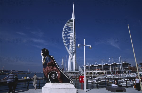 ENGLAND, Hampshire, Portsmouth, Gunwharf Keys. Spinnaker Tower with figurehead in the foreground. People on the waterfront promenade viewing the harbour.