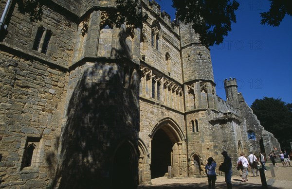 ENGLAND, East Sussex, Battle, Battle Abbey. Angled view of The Gatehouse seen from under tree branches with visitors walking through
