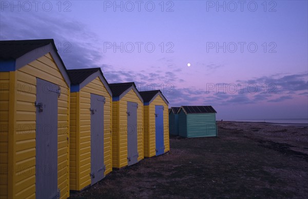 ENGLAND, West Sussex, Littlehampton, Row of  yellow and green beach huts next to promenade seen in evening light