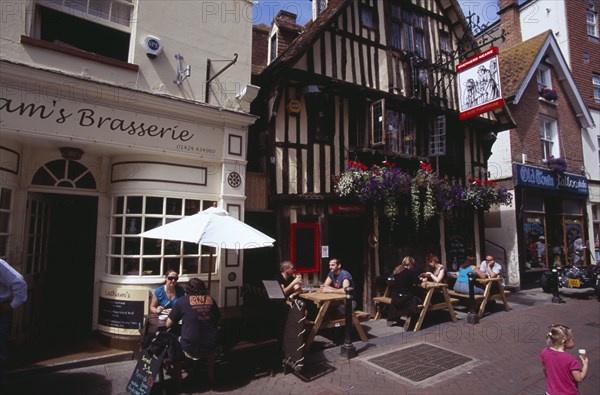 ENGLAND, East Sussex, Hastings, Old Town. George Street. Pubs and restaturants with people sitting at tables eating and drinking outside the timbered frontage of Ye Olde Pump House pub
