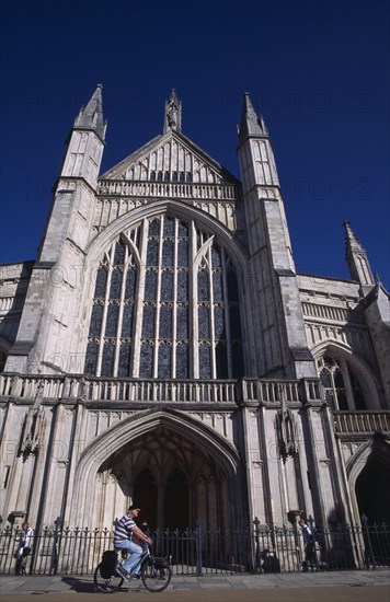 ENGLAND, Hampshire, Winchester, Winchester Cathedral exterior with a man travelling past on a bicycle