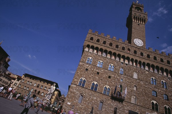 ITALY, Tuscany, Florence, Piazza della Signoria. Palazzo Vecchio with replica of the statue of David by Michelangelo .Tourists gathered on the ground