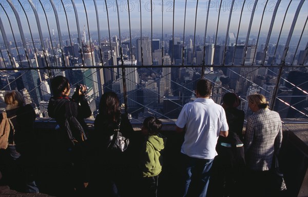 USA, New York, New York City, View north over city  from top of the Empire State Building at 8.30 a.m. with line of visitors looking out through expanse of glass.  One person using camcorder.