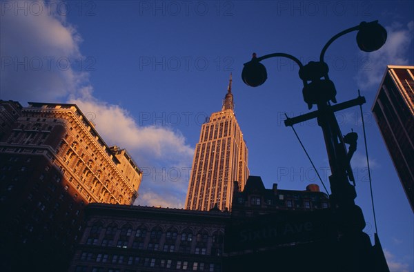 USA, New York, New York City, "Part view of the Empire State Building from 7th Avenue / West 31st Street in orange sunlight with silhouetted street light and buildings in deep shadow in foreground.   Designed by architect William Lamb of Shreve, Lamb and Harmon Associates.  Art Deco, steel framed with radio and TV mast completed in 1931."