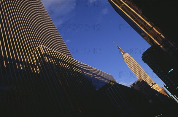 USA, New York, New York City, "Part view of the Empire State Building from West 31st Street.  Angled view seen in sunlight at end of street framed by buildings in foreground partly in shadow.   Designed by architect William Lamb of Shreve, Lamb and Harmon Associates.  Art Deco, steel framed with radio and TV mast completed in 1931."