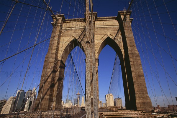 USA, New York, New York City, Brooklyn Bridge.  View along bridge to Manhattan skyline beyond part framed by central stone tower and intersected by steel wires and suspension cables. Spans the East River.  Construction began in 1870 and the bridge opened for use in 1883.