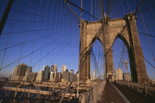 USA, New York, New York City, "Brooklyn Bridge.  View across bridge, pedestrians and cyclist to Manhattan skyline part framed by stone tower and intersected by steel wires and suspension cables. Spans the East River.  Construction began in 1870 and the bridge opened for use in 1883."