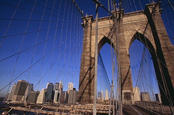 USA, New York, New York City, Brooklyn Bridge.  View across bridge towards Manhattan skyline part framed by stone tower and intersected by steel wires and suspension cables. Spans the East River.  Construction began in 1870 and the bridge opened for use in 1883.