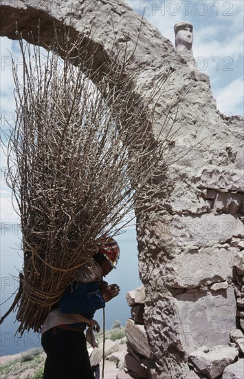 PERU, Puno, Lake Titicaca, Taquile Island.  Local man carrying bundle of twigs on his back framed in partly seen stone archway.