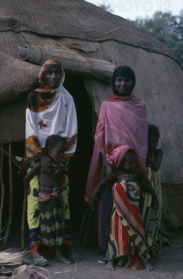 ETHIOPIA, North East, People, Afar women and children standing outside entrance of domed hut behind.