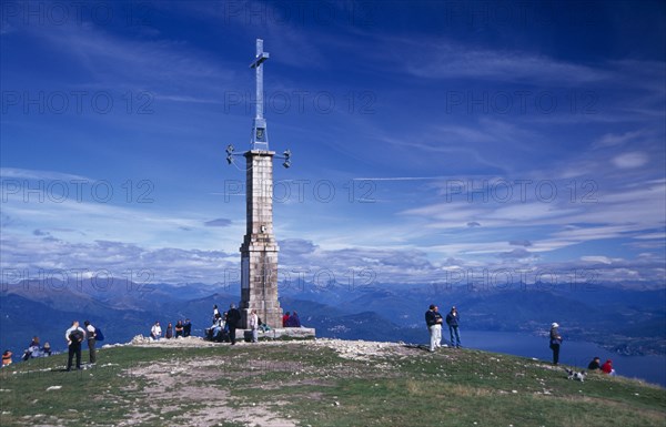 ITALY, Piedmont, Monte Mottarone, Tourists at summit of Monte Mottarone marked by tower and cross overlooking Lake Maggiore and the surrounding area.