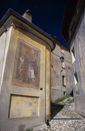 ITALY, Lombardy, Arcumeggia, Narrow cobbled street with fresco decoration on exterior wall of corner building.