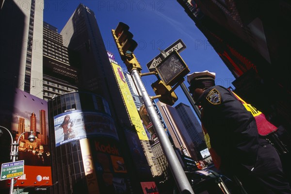 USA, New York, New York City, Times Square.  Angled view of traffic police officer standing below traffic lights and sign for pedestrian crossing surrounded by skyscrapers and advertising.