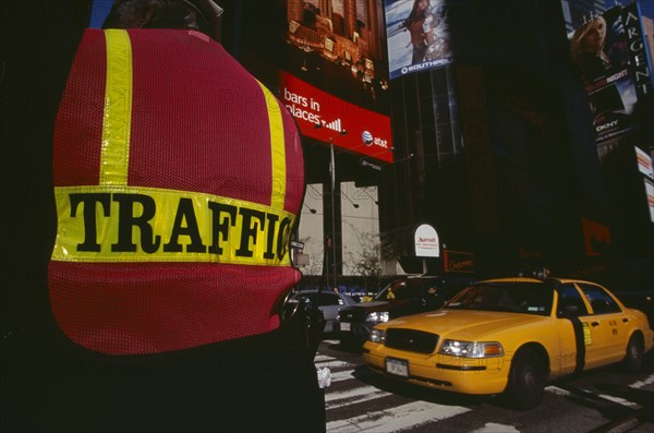 USA, New York, New York City, Times Square.  Traffic police officer wearing florescent jacket standing beside road with back to camera. Yellow taxi cab and other traffic waiting at pedestrian crossing.