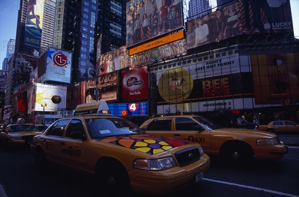 USA, New York, New York City, Times Square.  Yellow taxi cabs on street lined with skyscraper buildings and illuminated advertising in low light.