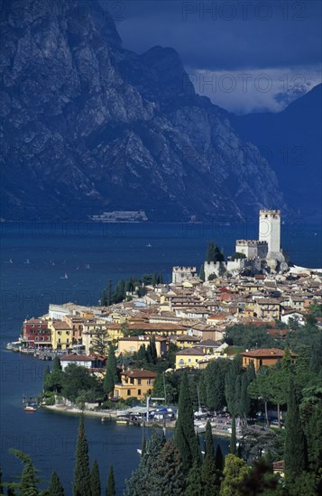 ITALY, Veneto, Lake Garda , Malcesine.  Tiled rooftops and pastel coloured buildings of town and castle on shore of lake with mountains beyond.