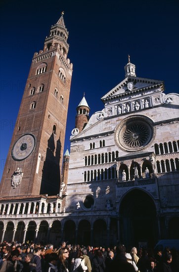 ITALY, Lombardy, Cremona, Piazza del Comune.  Part view of Duomo facade and medieval bell tower known as the Torrazzo linked by a Renaissance loggia.  Crowds of visitors in foreground.