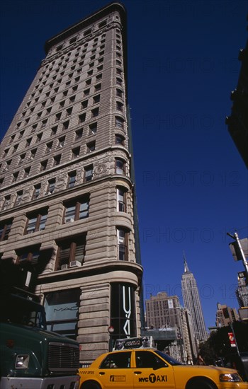USA, New York, New York City, "Angled view of the Flatiron Building from 23rd Street.  Traffic including yellow taxi cab below and Empire State Building beyond. Steel framed, Beaux-Arts skyscraper designed by architect Daniel Burnham in 1902 to a triangular plan. "