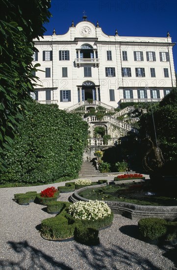 ITALY, Lombardy, Lake Como, Tremezzo.  Exterior facade and formal gardens of the Villa Carlotta.  Gravel pathway encircling fountain with tiered steps leading to entrance behind.