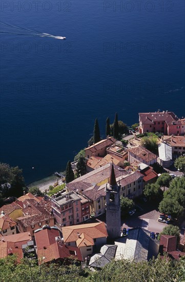 ITALY, Lombardy, Lake Como, "Varenna.  Looking down on red tiled rooftops, church and bell tower of town overlooking lake and distant speed boat."