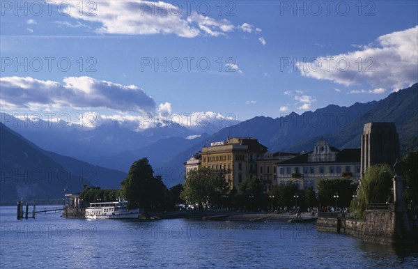ITALY, Piedmont, Lake Maggiore, "Pallanza.  Lakeside buildings, crowds and moored ferry boat with mountain backdrop."
