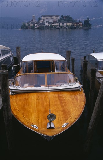 ITALY, Piedmont, Lake Orta, Moored boat taxi with small island densely covered with buildings behind.