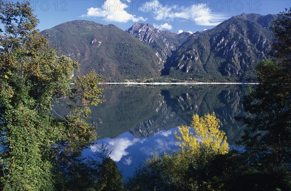 ITALY, Lombardy, Lake Iseo, Lago d’Iseo.  Trees and mountain landscape reflected in still surface of lake.