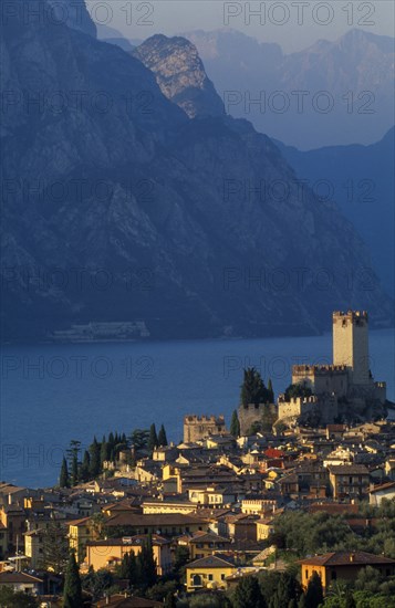 ITALY, Veneto, Lake Garda, "Malcesine.  View across town rooftops towards Castello Scaligero in warm, golden light with lake and mountains beyond."