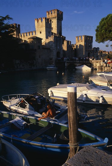 ITALY, Lombardy, Lake Garda , Sirmione.  Rocca Scaligera medieval castle with crowds of visitors crossing bridge to entrance.  Moored boats in foreground.
