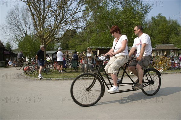 ENGLAND, West Sussex, Amberley, Amberley Working Museum. Veteran Cycle Day Grand Parade. Man and woman riding a riding a Tandem bicycle with visitors watching.