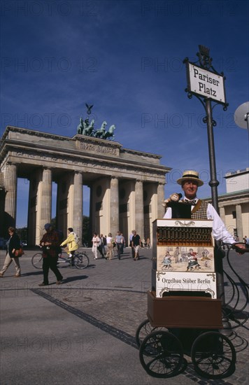 GERMANY, Berlin, Brandenburg Gate. Man in foreground under Pariser Platz sign performing with a Orgelbau Stuber Organ and a puppet monkey