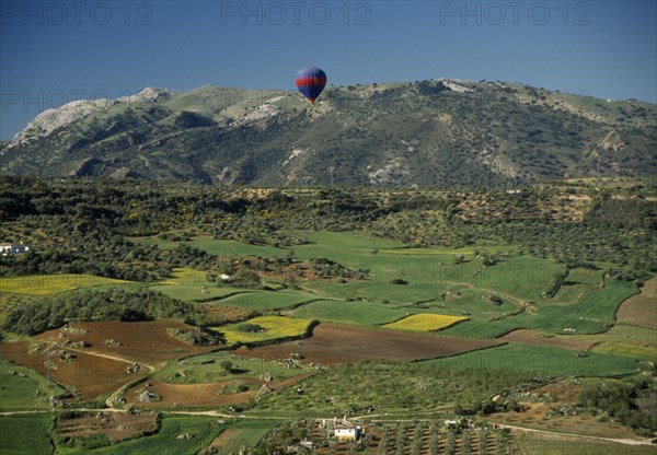 SPAIN, Andalucia, Malaga , A hot air balloon flying over green valley with patchwork fields towards mountain range