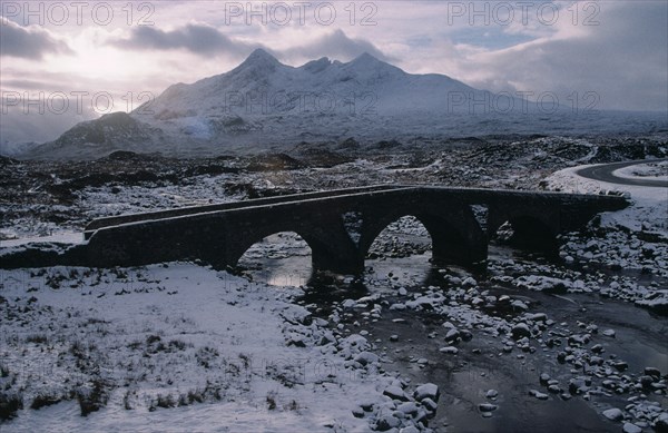SCOTLAND, Isle of Skye, Sligachan and the Cuillin Mountains in winter snow.  Narrow bridge over frozen river and grey sky.