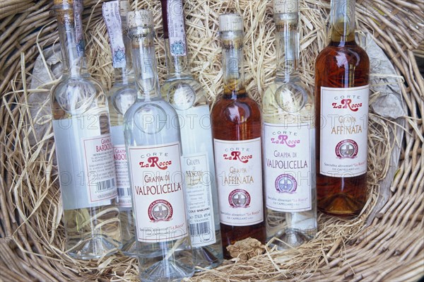 ITALY, Veneto, Lake Garda, Bardolino.  Selection of bottles of grappa displayed in basket.