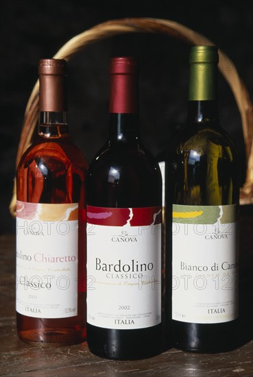 ITALY, Veneto, Lake Garda, "Bardolino.  Bottles of red, white and rose wine from the Bardolino region displayed in front of basket and framed by handle."