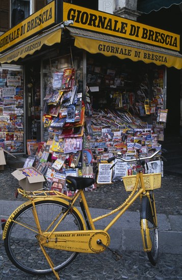 ITALY, Lombardy, Brescia, Piazza della Loggia.  Newspaper stand with yellow painted bicycle advertising name.