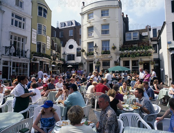 ENGLAND, East Sussex, Brighton, The North Lanes. East Street. People eating and drinking at tables outside busy restaurants and pubs