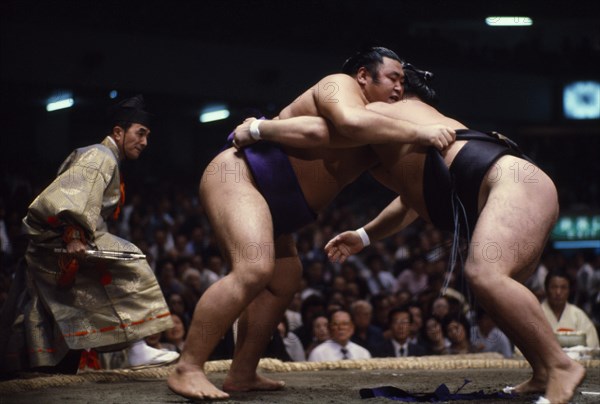 JAPAN, Samurai, Sumo, "Sumo wrestlers in ring watched by referee wearing the costume of a shogun.  Sumo is an ancient form of wrestling thought to have originated in Japan some 2,000 years ago.  The ring consists of a circle of clay set on a square mound and a bout is decided when any part of a wrestler’s body except the soles of his feet touches the ground or if he is pushed from the ring."