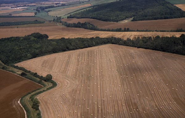 ENGLAND, Dorset, Agriculture, Aerial view over arable landscape and field patterns delineated by hedges with areas of trees and harvested field in foreground scattered with circular bales.