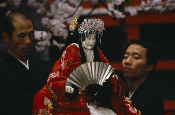 JAPAN, Arts, Performance, "Bunraku puppet female character with puppeteers.   Puppet is half life size, dressed in red, embroidered kimono and holding fan. "