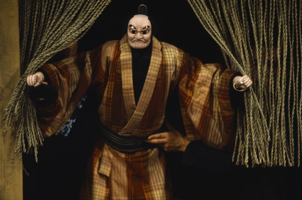 JAPAN, Arts, Performance, Bunraku puppet male character appearing from behind curtains with puppeteer partly seen at side.