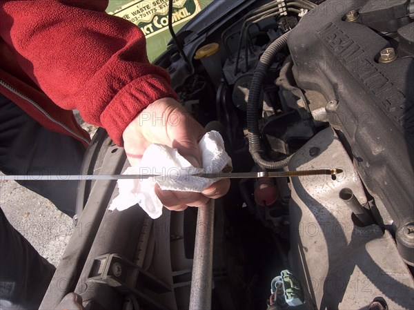 TRANSPORT, Road, Cars, Man checking oil level on the car engine dipstick and wiping it on a white paper tissue