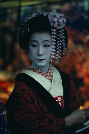 JAPAN, Customs, Geisha, "Three-quarter portrait of sixteen year old Someiyu, a maiko or apprentice geisha with white powdered face and red painted lips wearing richly patterned kimono and hair decoration. "