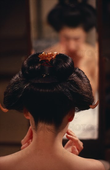 JAPAN, Customs, Geisha, "Head of geisha seen from behind to show hairstyle with mirror reflection beyond.  Wigs may be used on special occasions, but geisha and maiko usually fix their own hair into an elaborate style known as ‘split peach’.  When they sleep the girls rest their heads on wooden pillows so as not to disturb the shape of the hair."