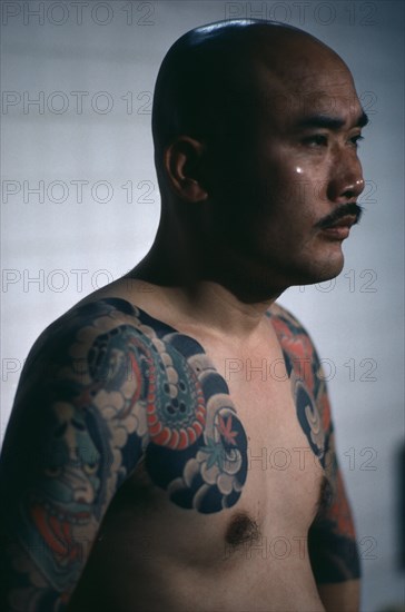 JAPAN, People, Yakuza, Three-quarter shot of gangster or Yakuza gang member in public bath house showing tattoo extending over shoulder and upper arm.  Tattoos are chosen to depict inspiring ideals of heroism and romance inherent in Japanese mythology.