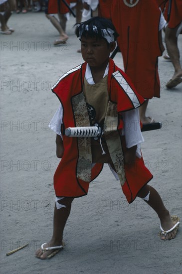 JAPAN, Kyushu, Kaseda Shrine, Young boy wearing traditional costume and carrying short sword at village festival.  In feudal times Kyushu was notable for the power of its great daimyo families and the festival celebrates the samurai with traditional dance and displays of martial arts.
