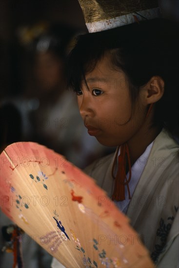 JAPAN, Kyushu, Kaseda Shrine, "Portrait of young shrine maiden employed to welcome visitors, supervise offerings and perform sacred dances for the Shinto gods or kami.  Head and shoulders, three-quarter portrait to left, carrying painted fan."